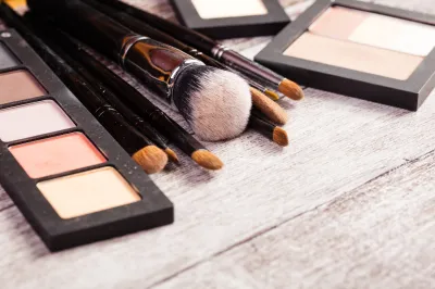 Make up brushes with cosmetics products next to them in close up photo on wooden background